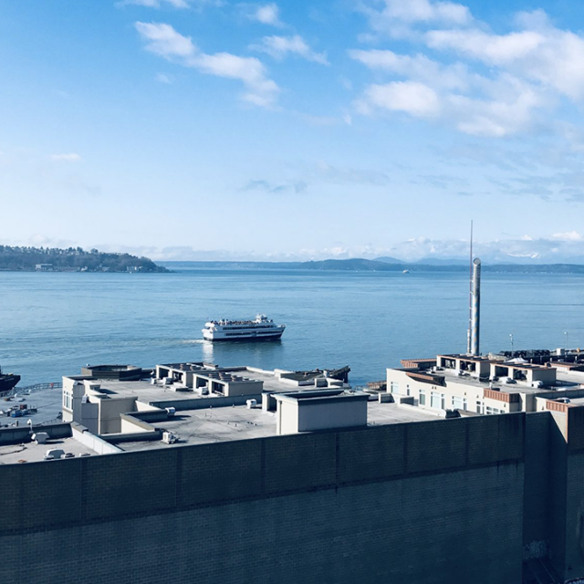 large body of blue water with mountains in the distance and a large industrial gray building near the camera person in the foreground