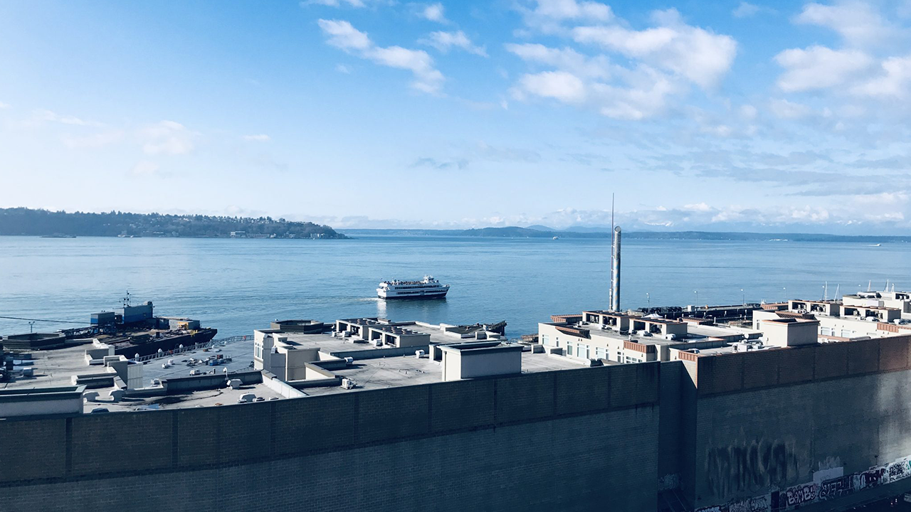 large body of blue water with mountains in the distance and a large industrial gray building near the camera person in the foreground